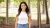 Young woman wearing white blouse and denim jeans, smiling and standing in woodland